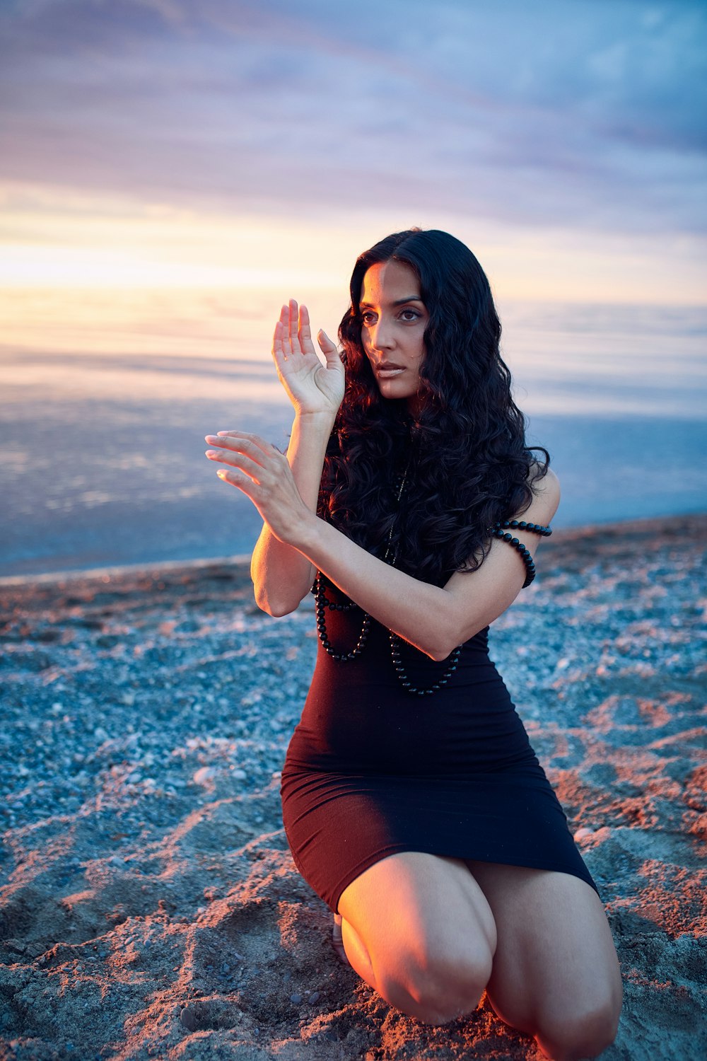 a woman kneeling on a beach with her hands together