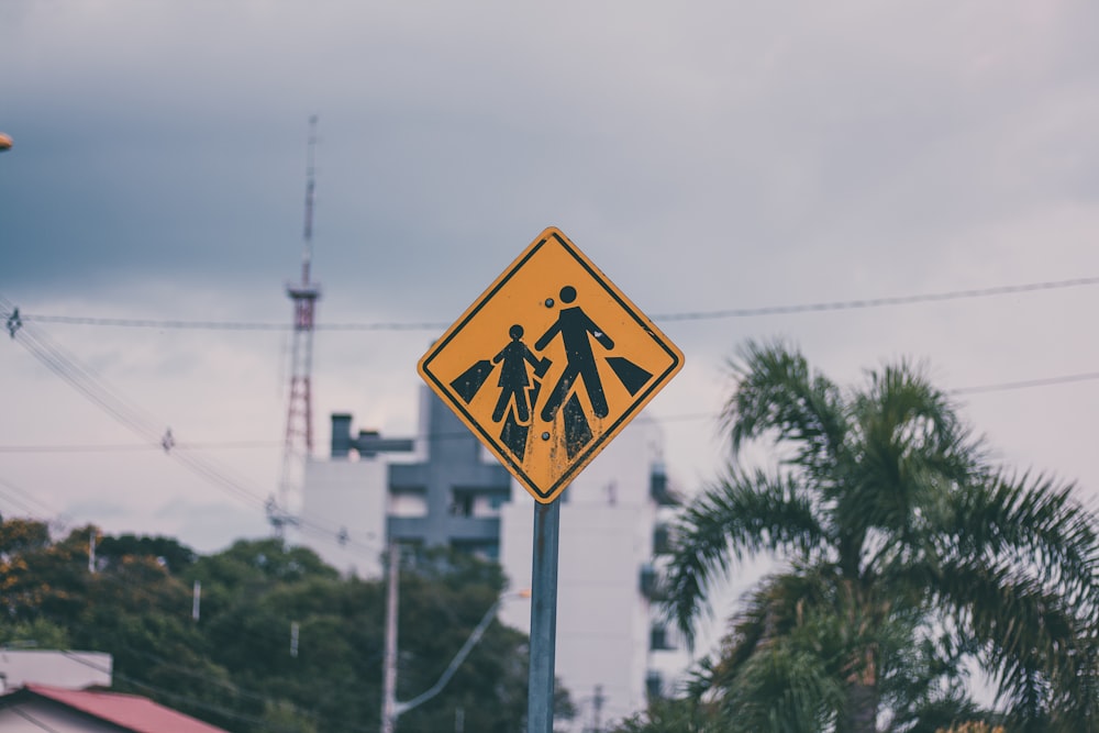 a yellow pedestrian crossing sign sitting on the side of a road