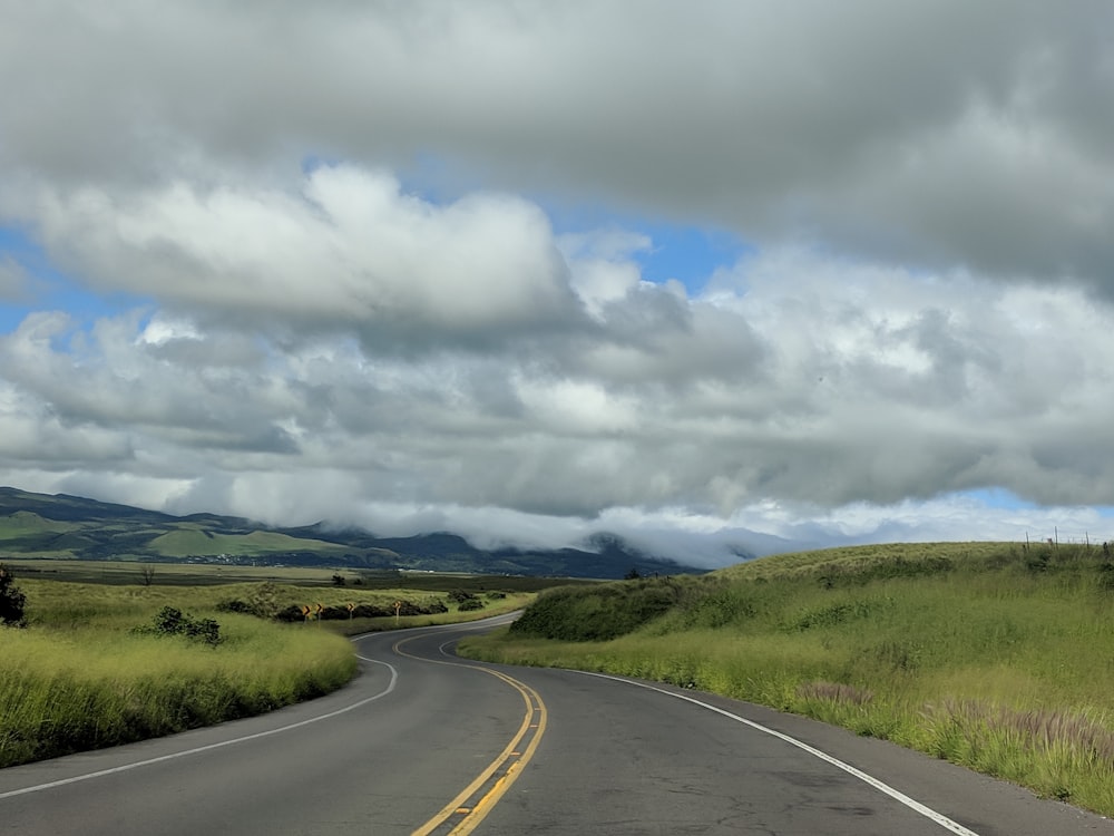 an empty road in the middle of a grassy field