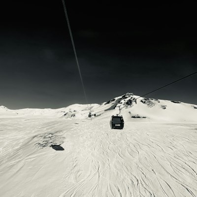 A gondola cabin on its cable climbing a broad snowy ridge in flat grey light at Laax, with ski tracks on the slope below