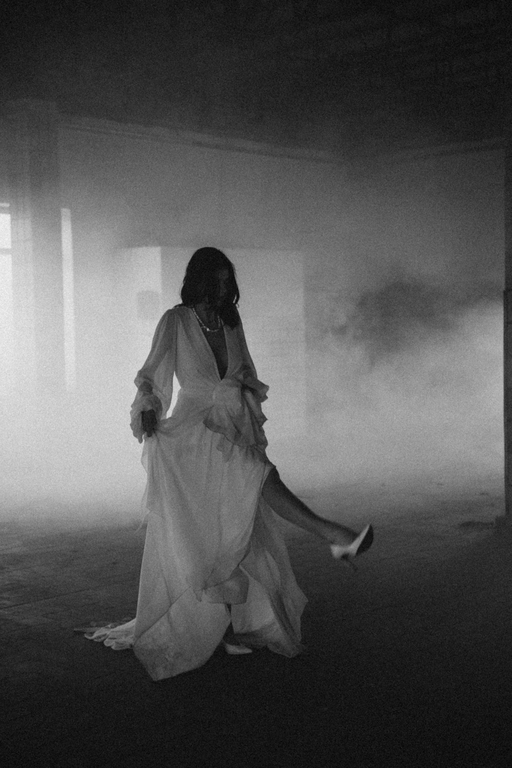 a woman in a long white dress walking through a foggy room