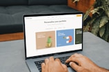 A person is typing on a MacBook Pro, viewing a website titled 'Personalize your portfolio.' The webpage displays three sections related to investing, each with different images and text. The laptop is on a grey table with a dark sofa and indoor plants in the background.