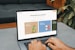 A person is typing on a MacBook Pro, viewing a website titled 'Personalize your portfolio.' The webpage displays three sections related to investing, each with different images and text. The laptop is on a grey table with a dark sofa and indoor plants in the background.