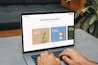 A person is typing on a MacBook Pro, viewing a website titled 'Personalize your portfolio.' The webpage displays three sections related to investing, each with different images and text. The laptop is on a grey table with a dark sofa and indoor plants in the background.