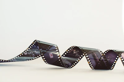 A length of photographic film is loosely coiled and displayed in a wave-like pattern. The film displays a series of images in muted colors against a soft white background.