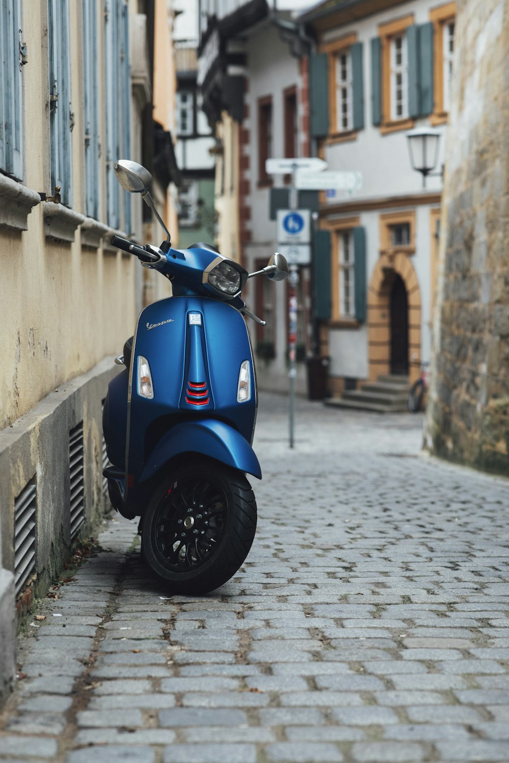 a blue scooter parked on a cobblestone street