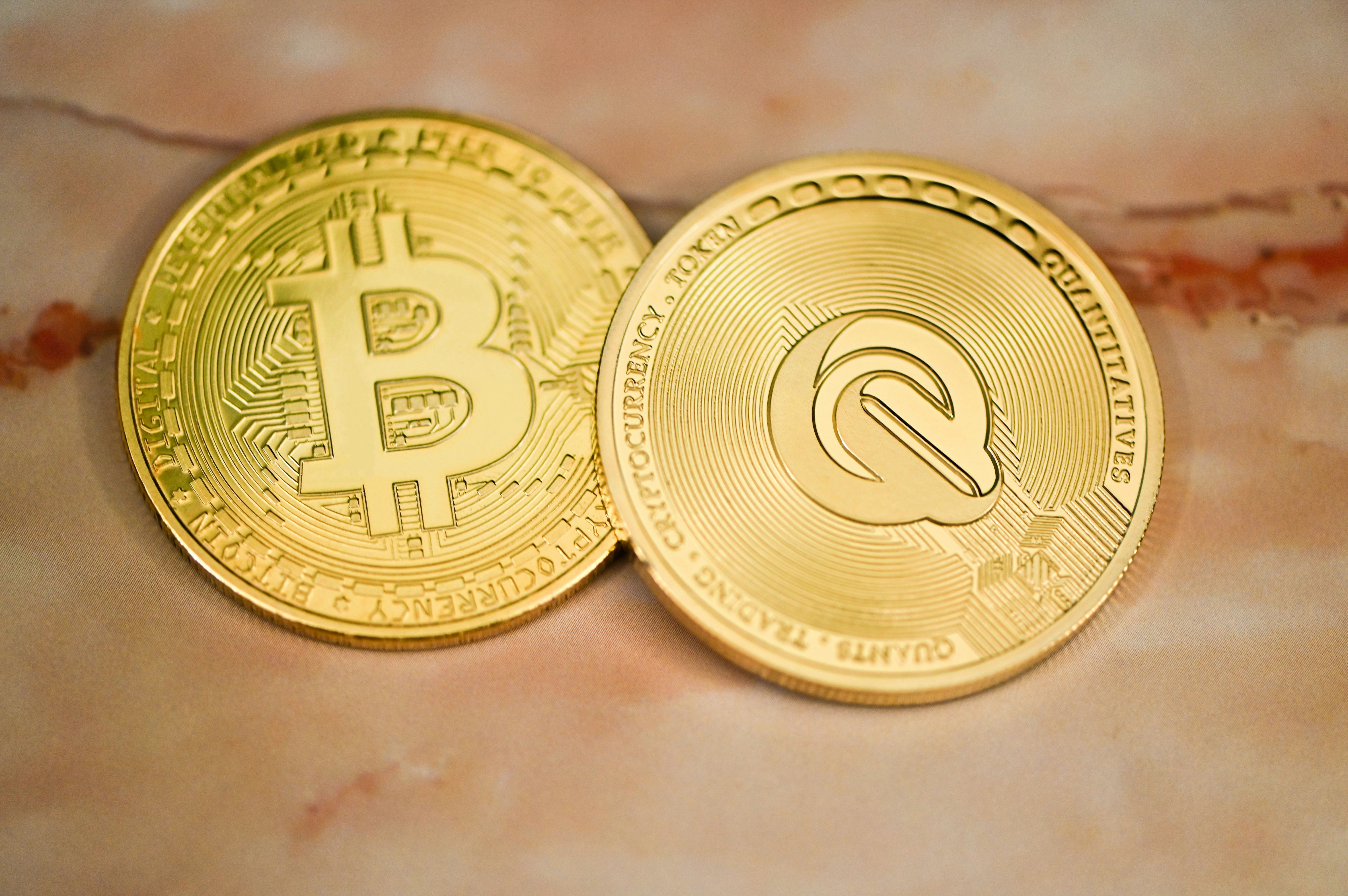 Bitcoin and QEST coin placed on a pink marble background