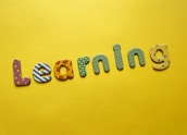 Colorful, decorative letters spelling 'Learning' are arranged across a bright yellow background. Each letter has a different pattern, including stripes, polka dots, flowers, and stars.