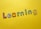 Colorful, decorative letters spelling 'Learning' are arranged across a bright yellow background. Each letter has a different pattern, including stripes, polka dots, flowers, and stars.