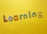 Colorful, decorative letters spelling 'Learning' are arranged across a bright yellow background. Each letter has a different pattern, including stripes, polka dots, flowers, and stars.