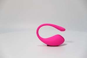 A modern, sleek pink object with a curved design sits against a plain, light-colored background. The object appears to be made of smooth material and is designed for a contemporary look.