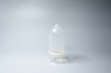 A transparent condom is placed upright against a plain light gray background. The image is minimalistic with the condom being the central focus.