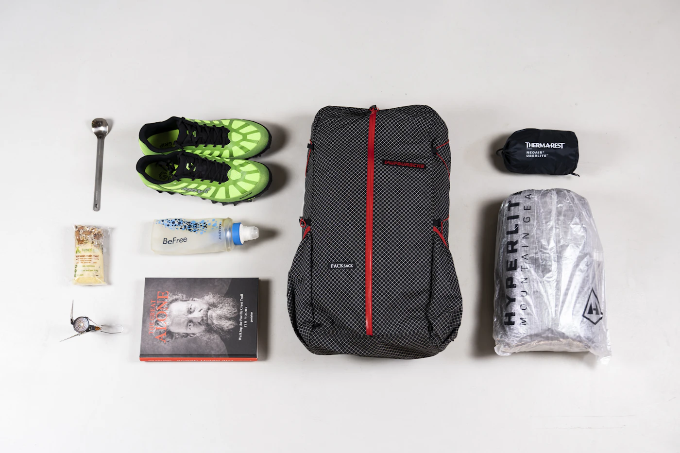 Tramping pack contents laid out flat on a wooden floor — jacket, pack, stove, sleeping mat