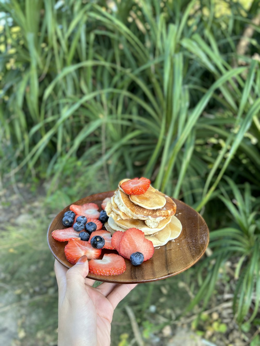 a person holding a plate of pancakes and strawberries