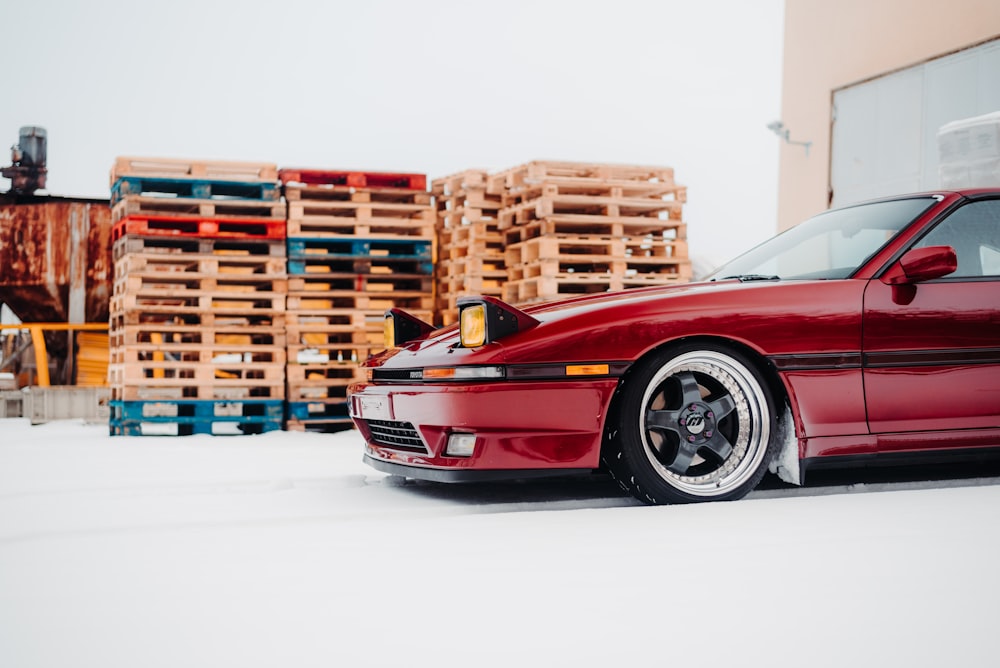 a red car parked in front of a pile of pallets