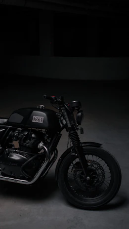 A sleek black motorcycle parked under moody lighting, emphasizing its design details.