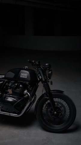 A sleek black motorcycle parked in a minimalist industrial space with warm light casting long shadows.