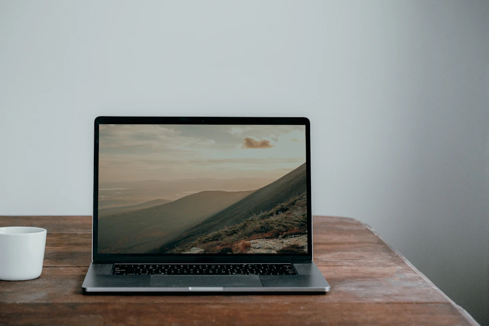 Laptop on a wooden table displaying a mountain landscape.