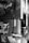 A black and white photograph features a vintage film camera hanging from a strap on a wooden surface. To the left, a sign with stylized text reads 'Love Sex & Magic'. Behind the camera and sign, part of a painting or art piece is partially visible, depicting abstract objects and shapes.