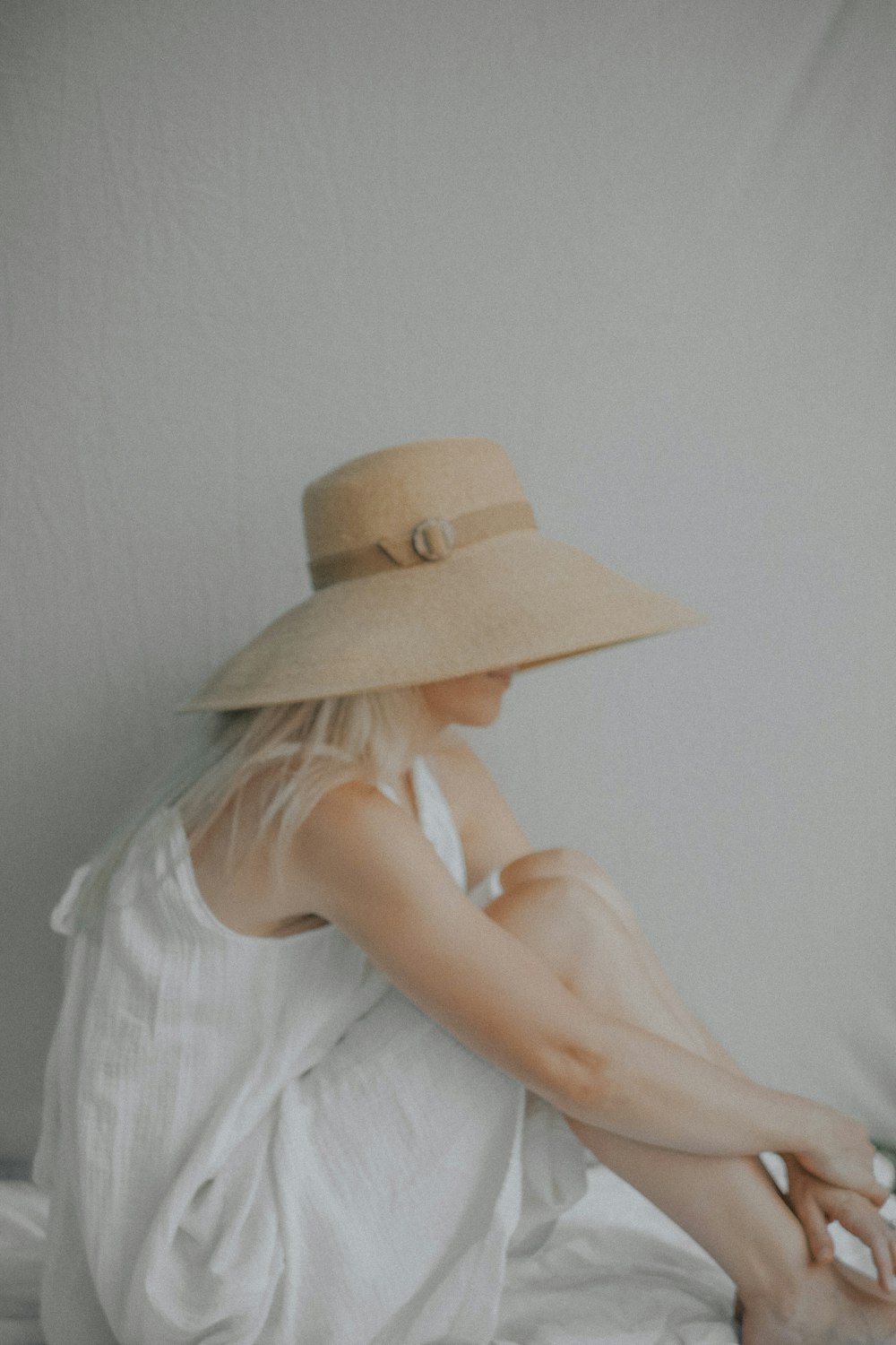 a woman sitting on a bed wearing a hat