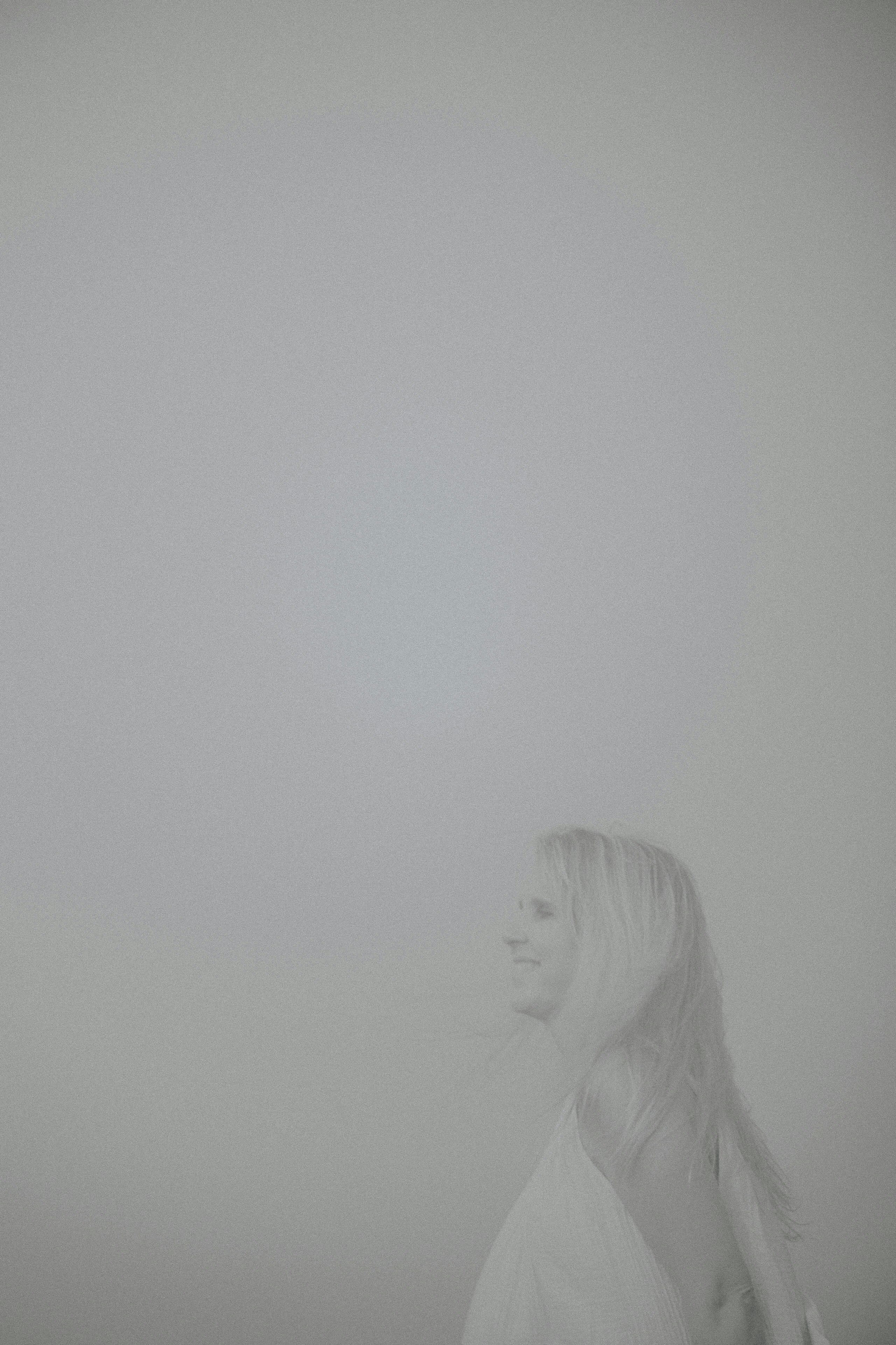 a woman standing in the fog with her hair blowing in the wind