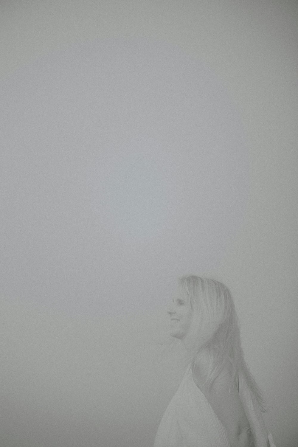 a woman standing in the fog with her hair blowing in the wind