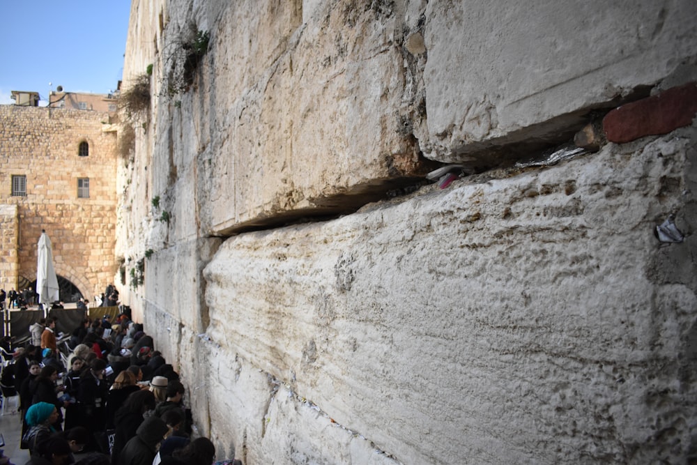 a crowd of people standing next to a stone wall