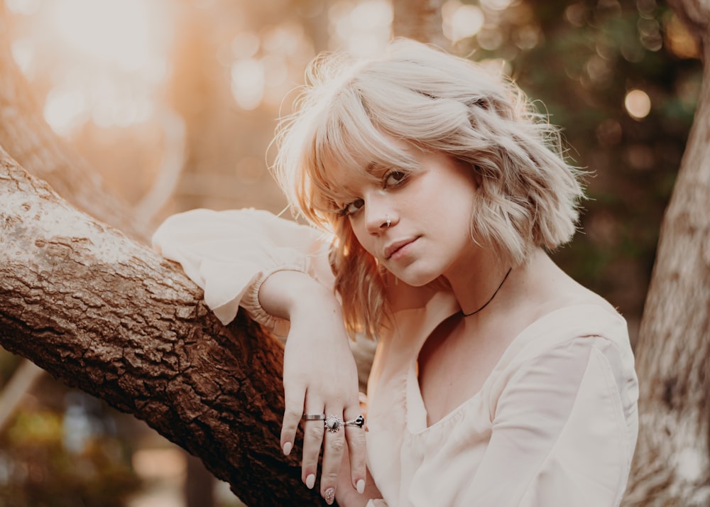 a woman leaning on a tree branch with her hand on her shoulder