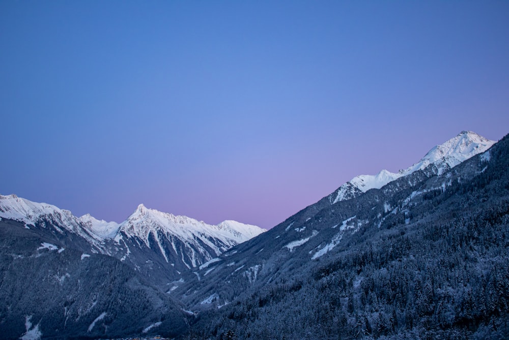 a view of a snowy mountain range at dusk