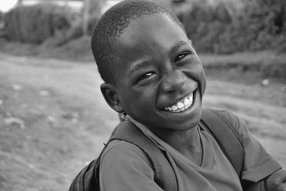 a young boy smiles while sitting on the side of a road