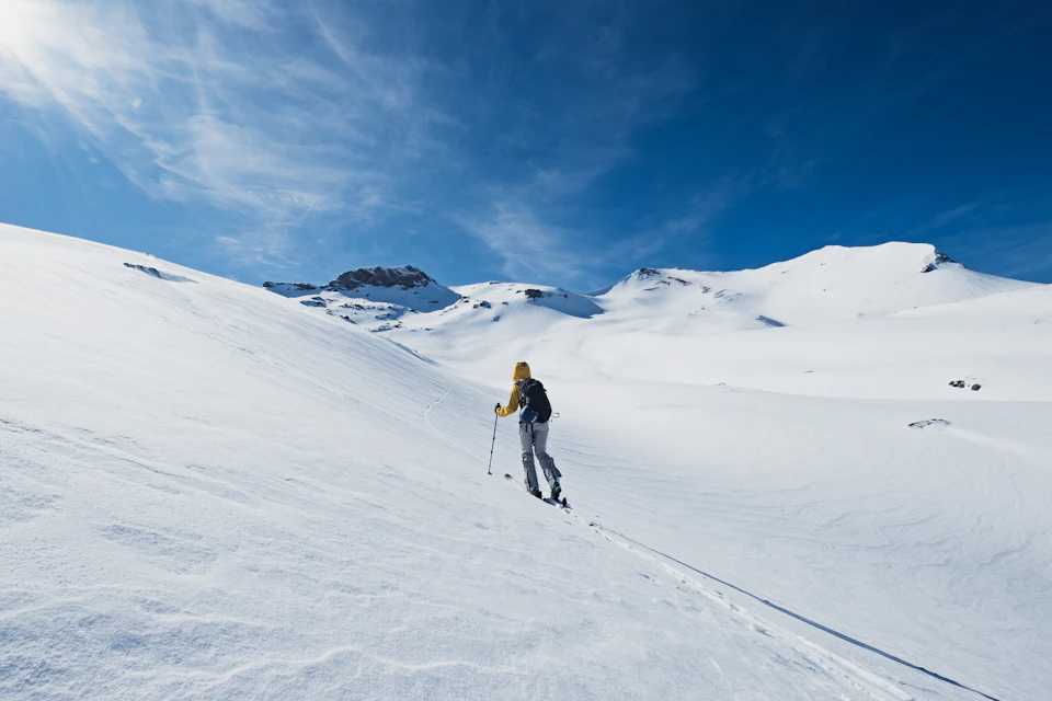 Lone skier in black jacket and gray pants skiing down steep snowy slope