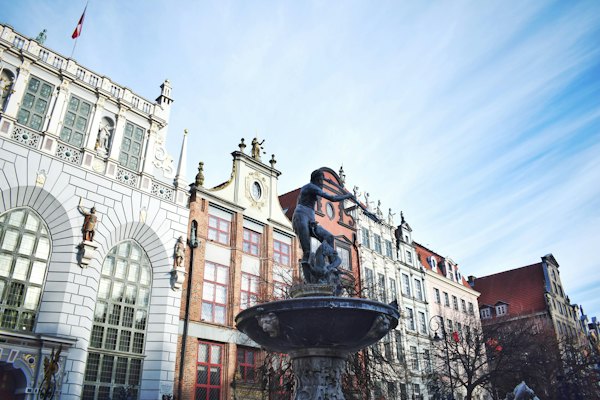 A statue of a man on a fountain in front of a building — Gdańsk, Poland
