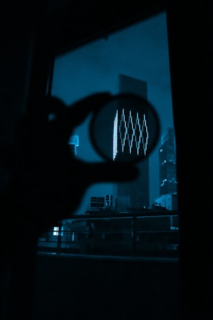 A silhouette of a detective holding a magnifying glass against a backdrop of city lights at night.