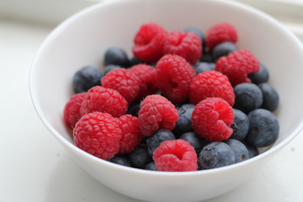 un bol blanc rempli de framboises et de bleuets