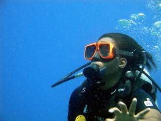 A scuba diver is submerged underwater, wearing an orange dive mask and a scuba suit, with air bubbles rising to the surface.