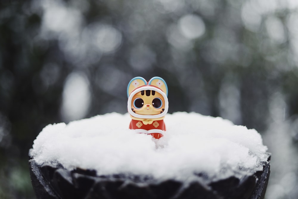 uma pequena estatueta sentada em cima de uma pilha de neve