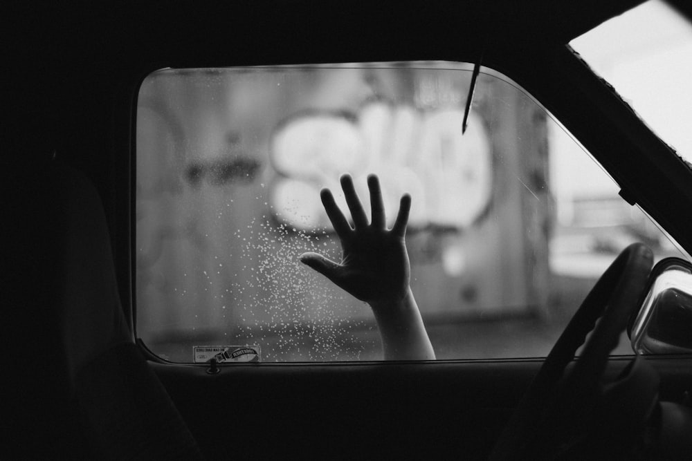 a black and white photo of a person's hand out of a car window