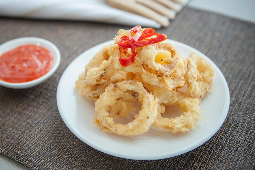 a white plate topped with onion rings next to a bowl of ketchup