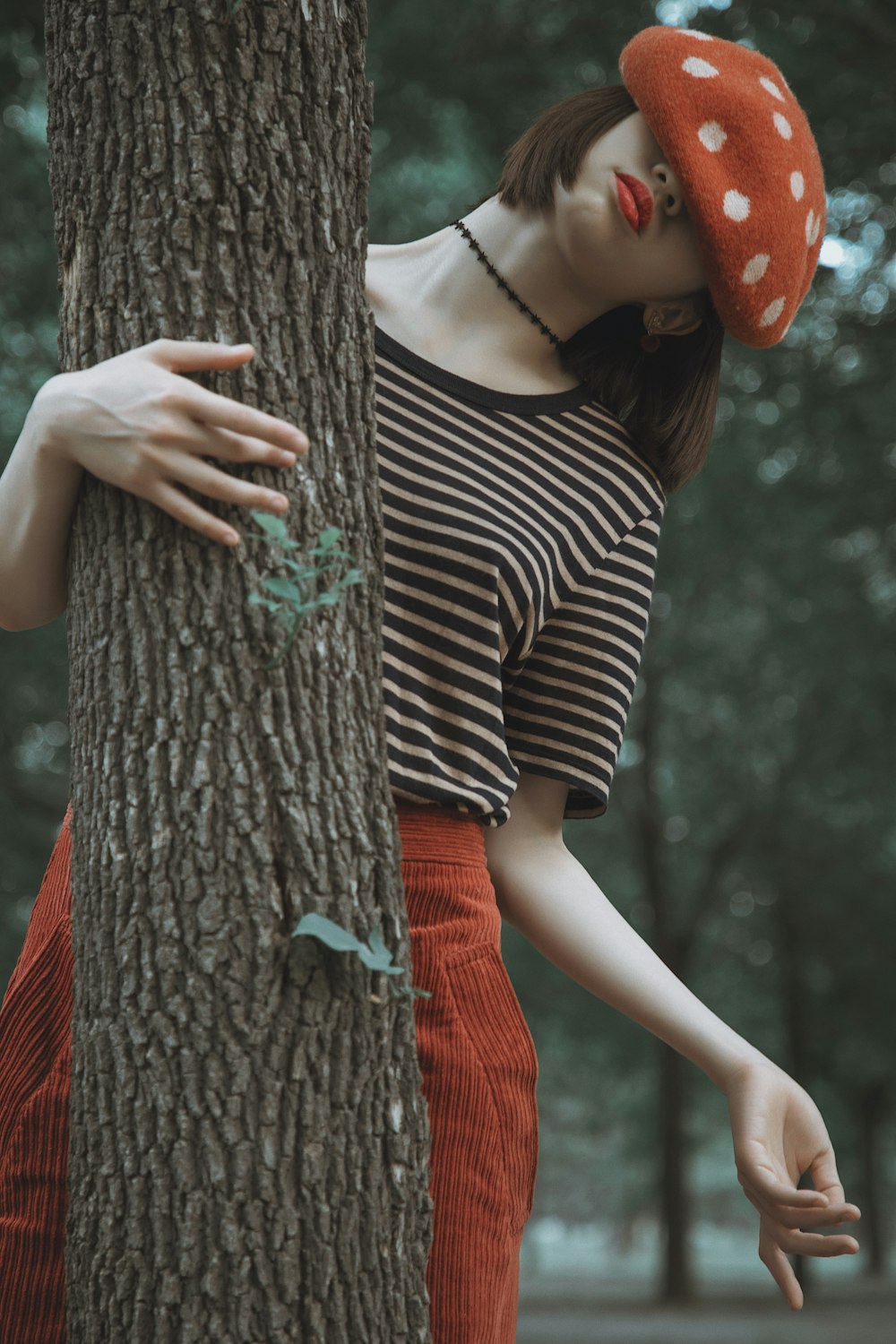 a woman leaning against a tree wearing a red hat