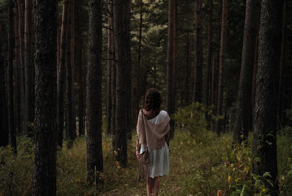 a woman in a white dress walking through a forest