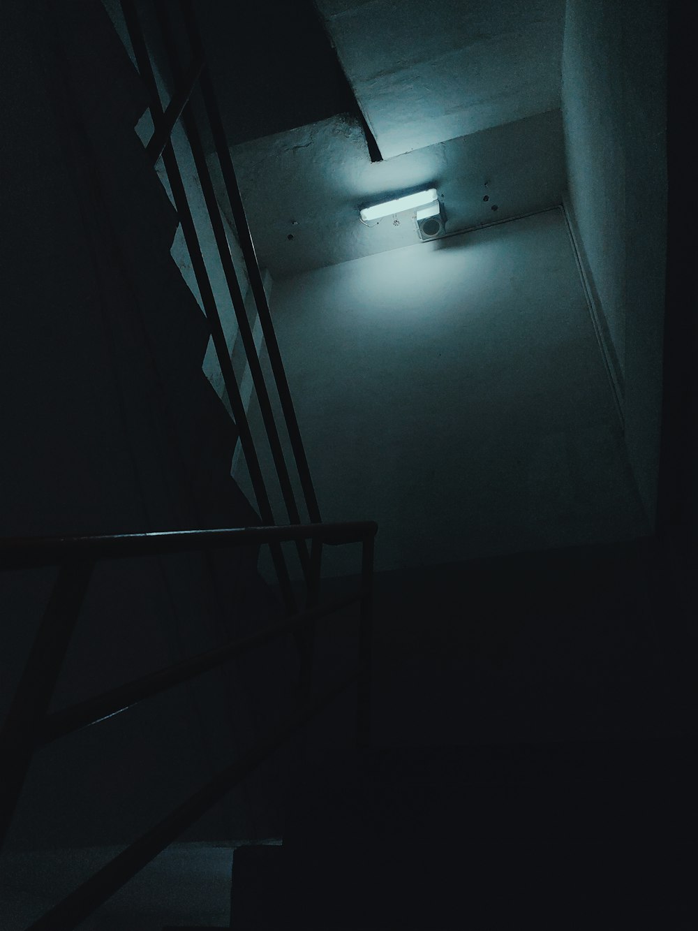 a dark hallway with stairs and a light at the end
