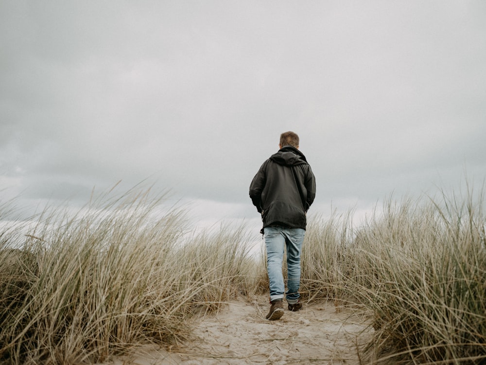 a man in a black jacket walking through tall grass