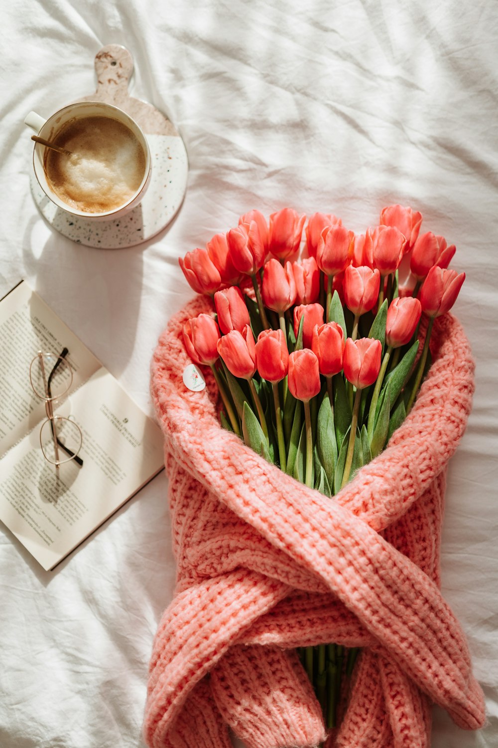 a bouquet of red tulips wrapped in a blanket next to a cup of