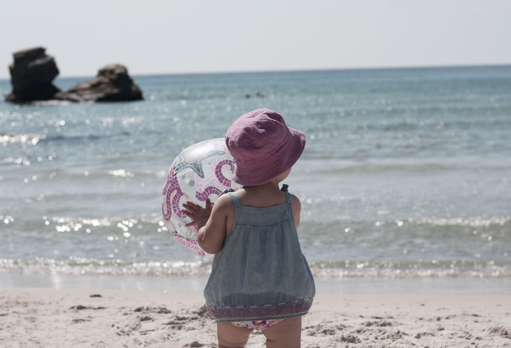una bambina in piedi su una spiaggia che tiene una palla