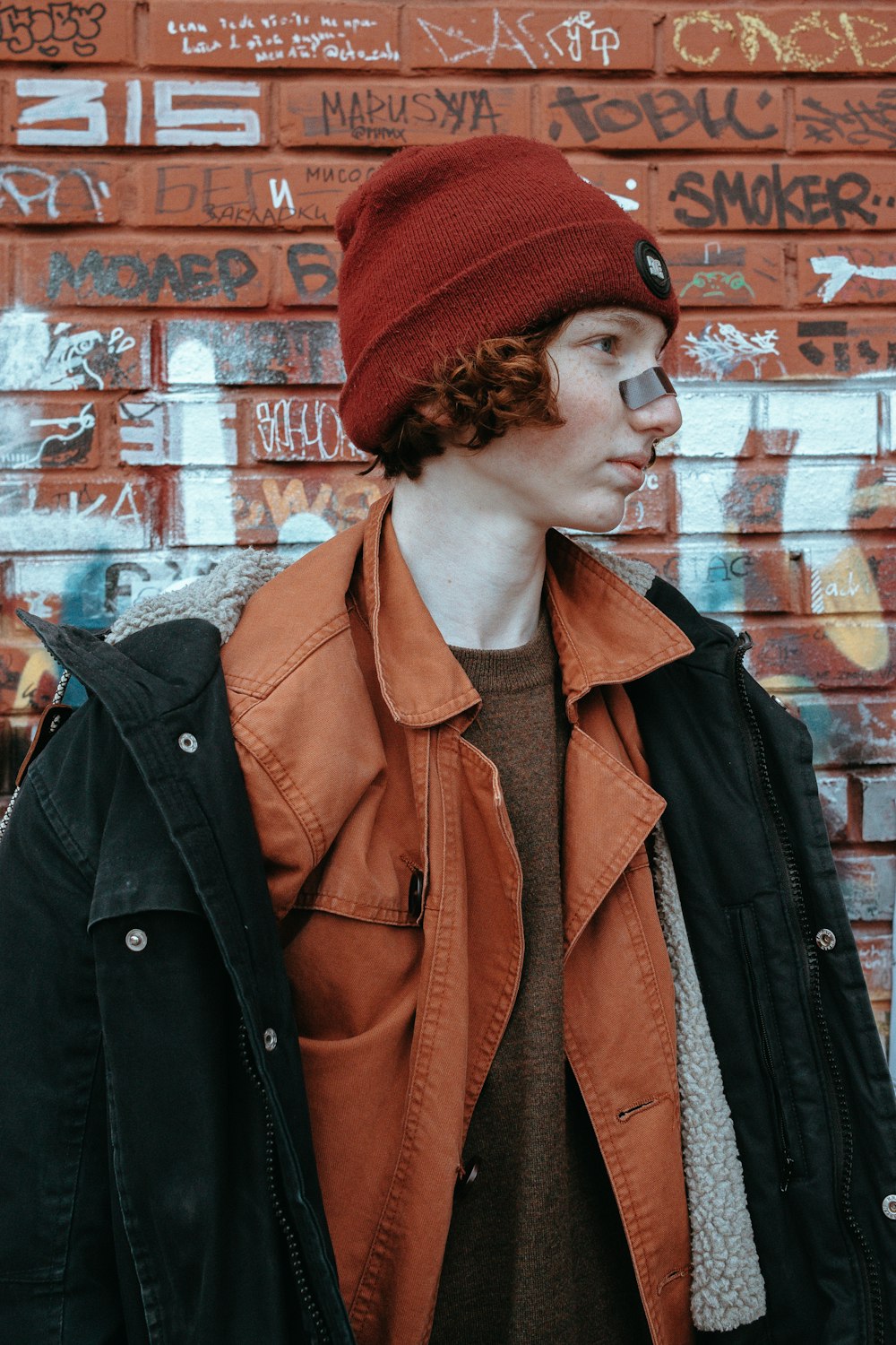 a young man wearing a red beanie standing in front of a brick wall