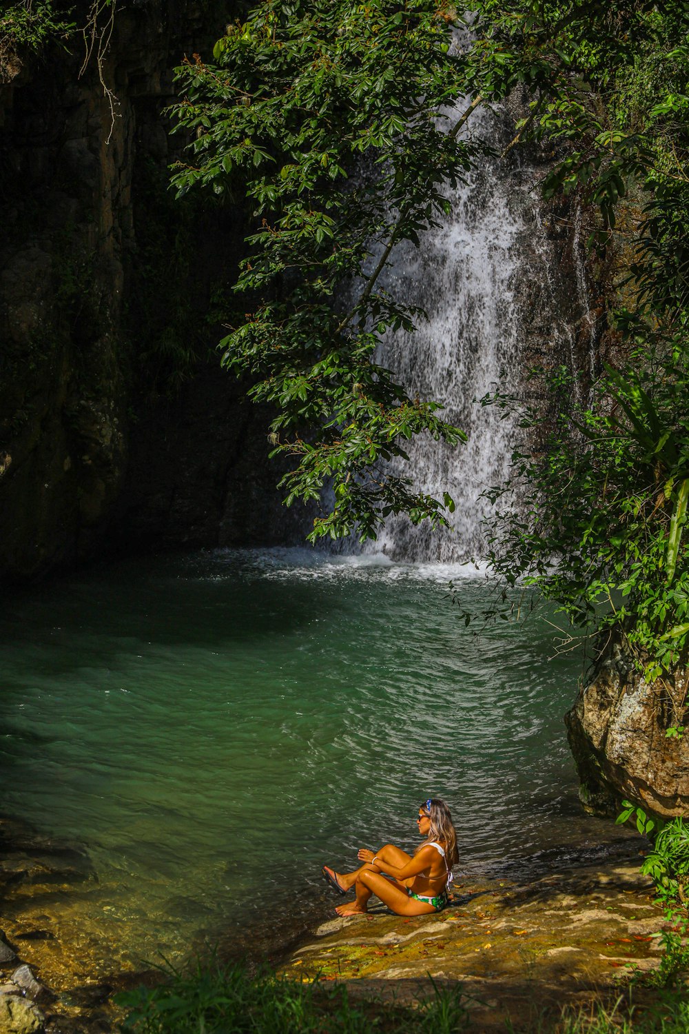 a woman sitting on a rock in front of a waterfall