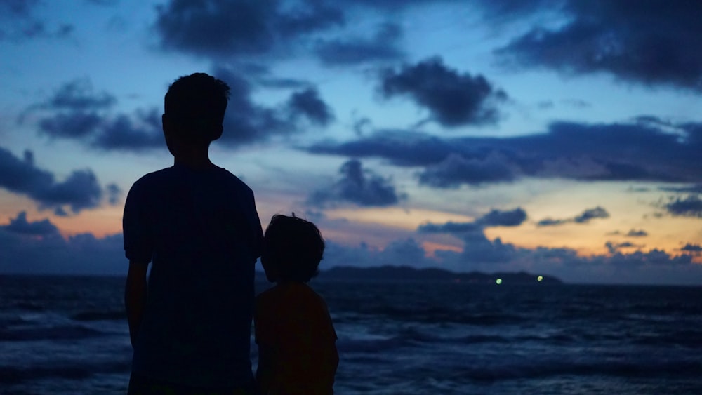 a man and a child standing on a beach watching the sunset