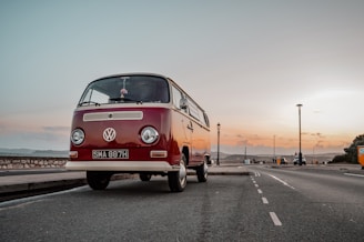 Wide-angle photo capturing a row of vintage Volkswagen vans parked along a scenic coastal road at sunset.