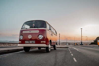 Wide-angle photo capturing a row of vintage Volkswagen vans parked along a scenic coastal road at sunset.