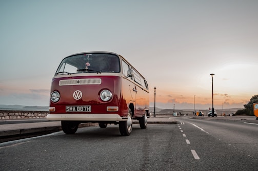 A vibrant red Volkswagen van parked by a serene lakeside at sunset.